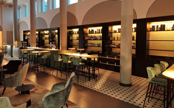 Bar und Lounge mit beleuchteten Regalen und grünen Sitzmöbeln