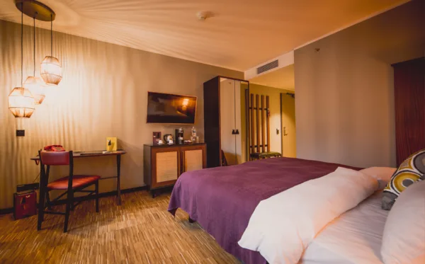 Hotelzimmer mit Bett, Schreibtisch und warmen Pendelleuchten